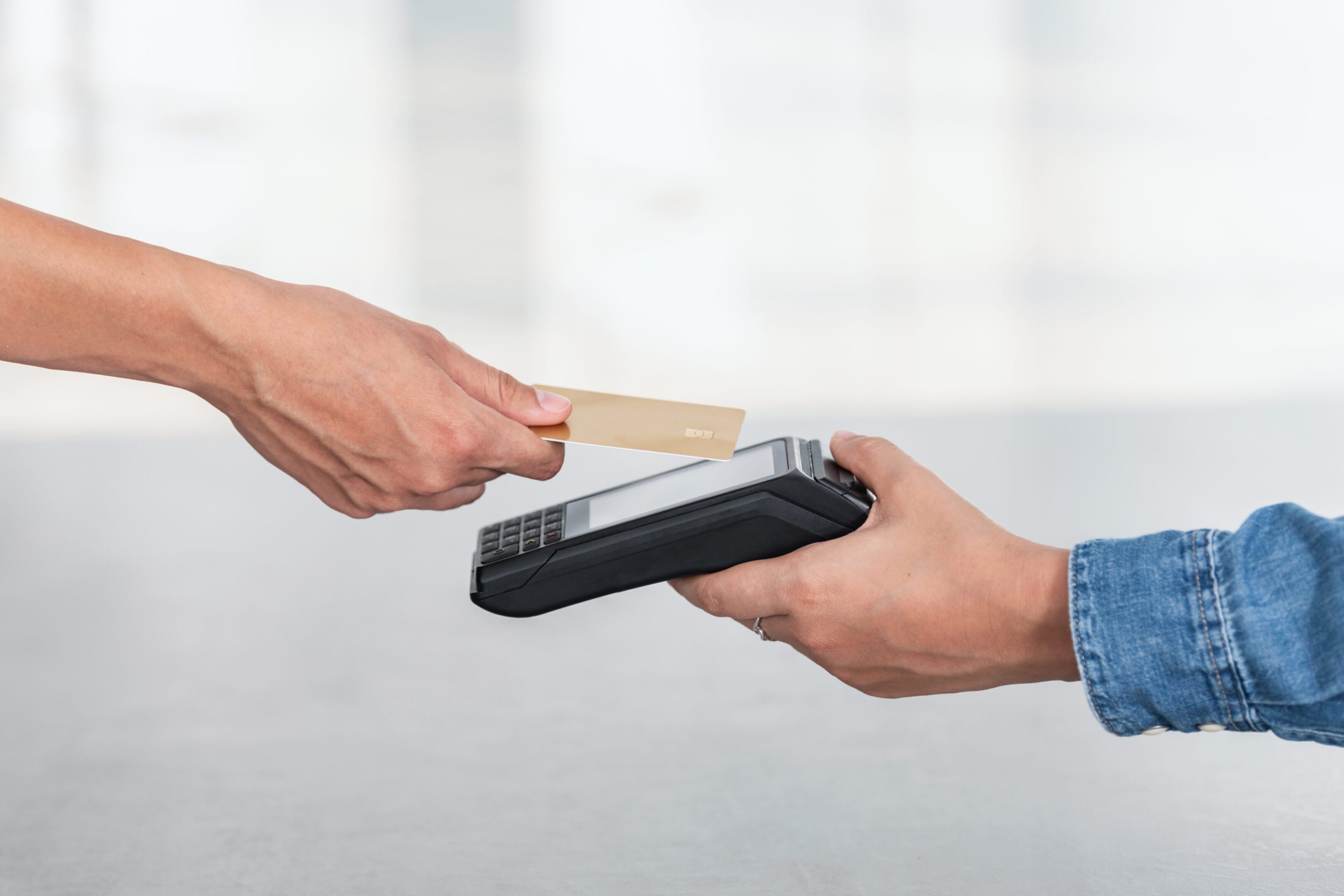 A hand holding a credit card near a card reader for payment.